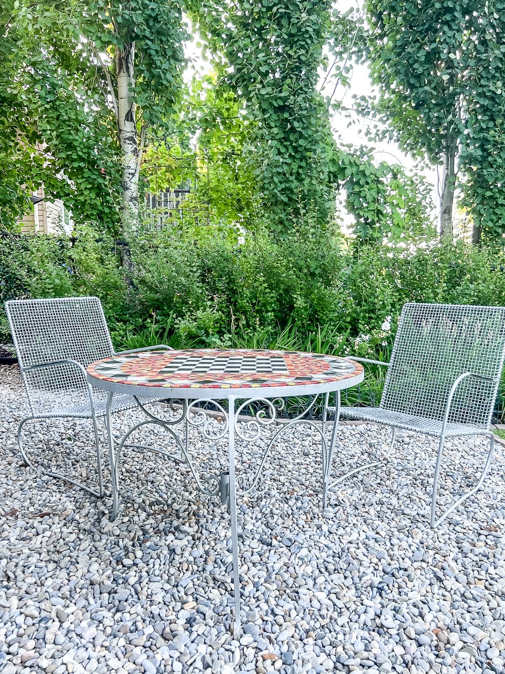 A graveled area in the garden with around table and two chairs to create an easy diy outdoor sitting area