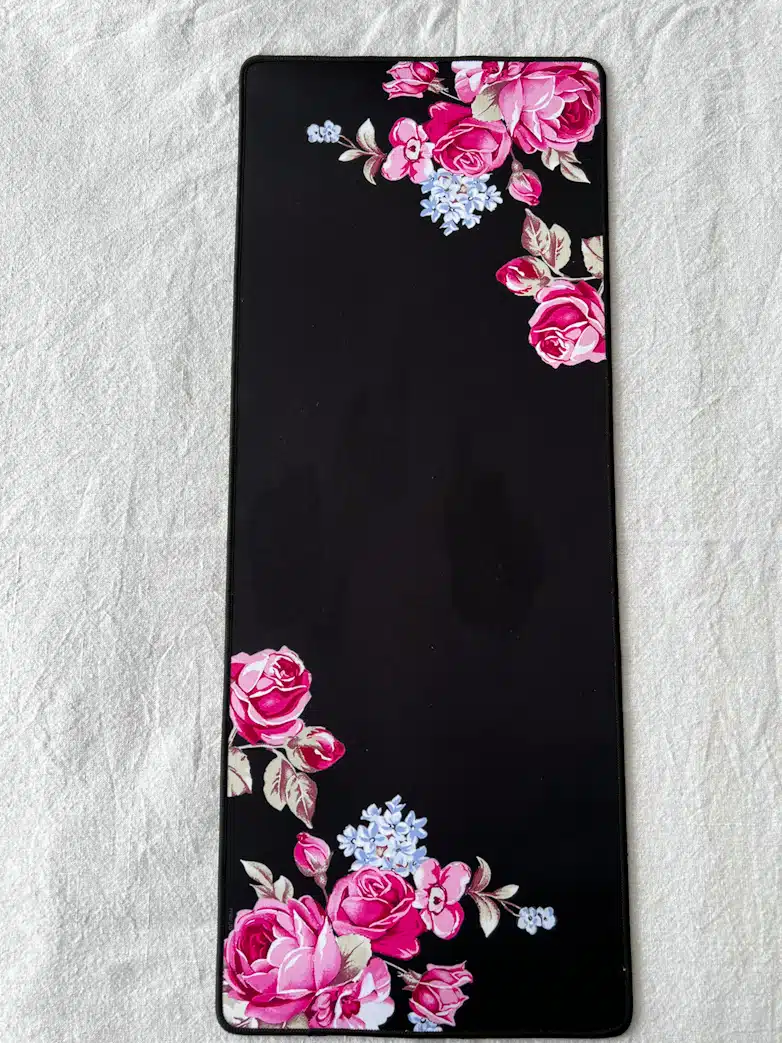 A desk pad or oversized mouse pad in black with bright pink roses decorating the corners