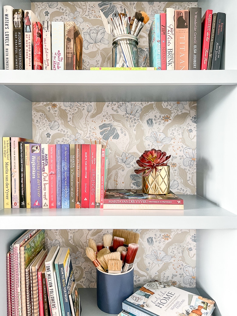 Decorating bookcases with books and a variety of paintbrushes in containers
