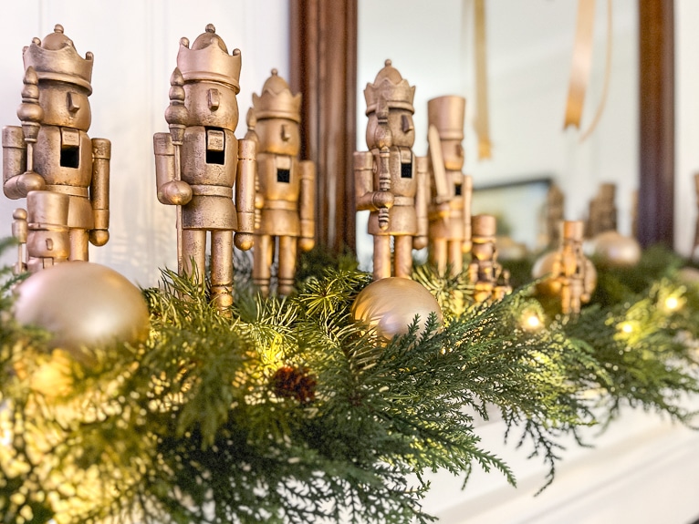 Faux brass nutcrackers and greenery on a white mantel.