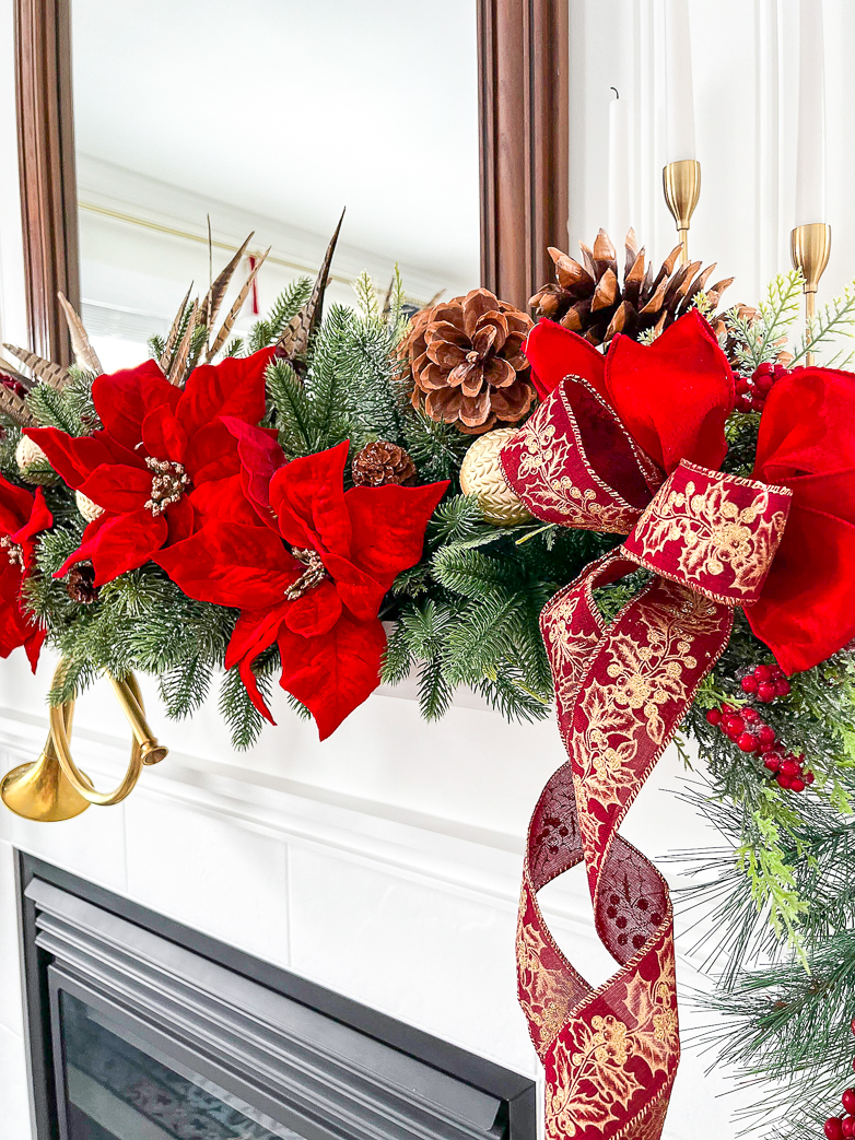 Mantel decor with big red faux poinsettias, garland and red ribbon and bows